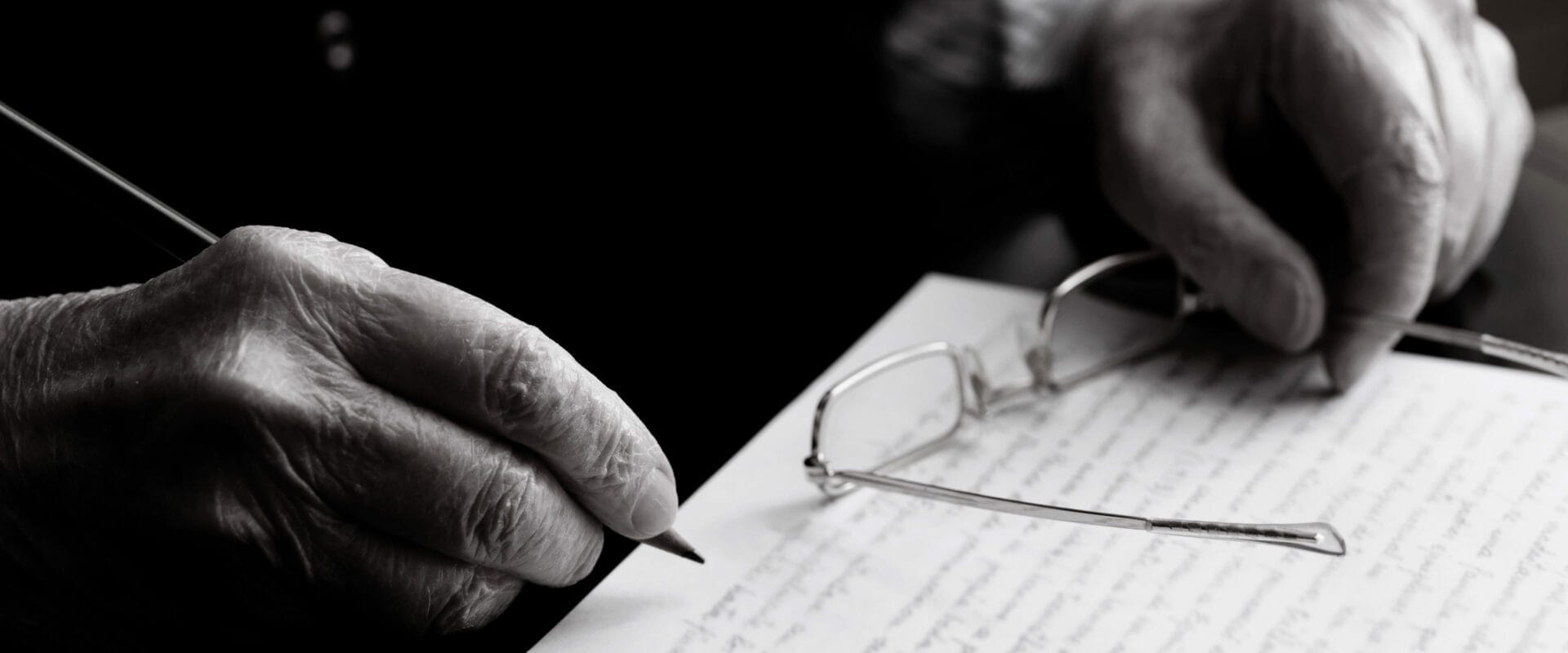 Male hands signing a contract with glasses one hand and a pen in the other.