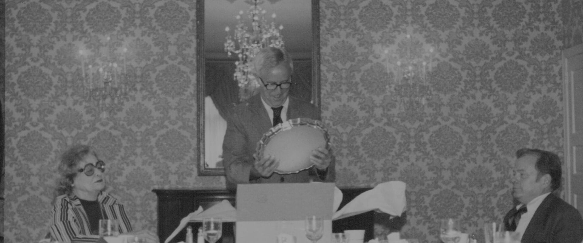 Former HWP owner is pictured center opening a gift at the head of the table. A woman is seated to the left and Howard W. Phillips Jr. is seated to the right.