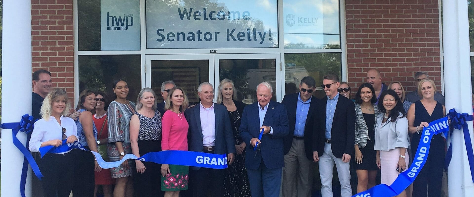 A mix of staff and local community member pictured in front of the Hughesville Office. Senator Kelly is pictured in the center cutting the grand opening ribbon.